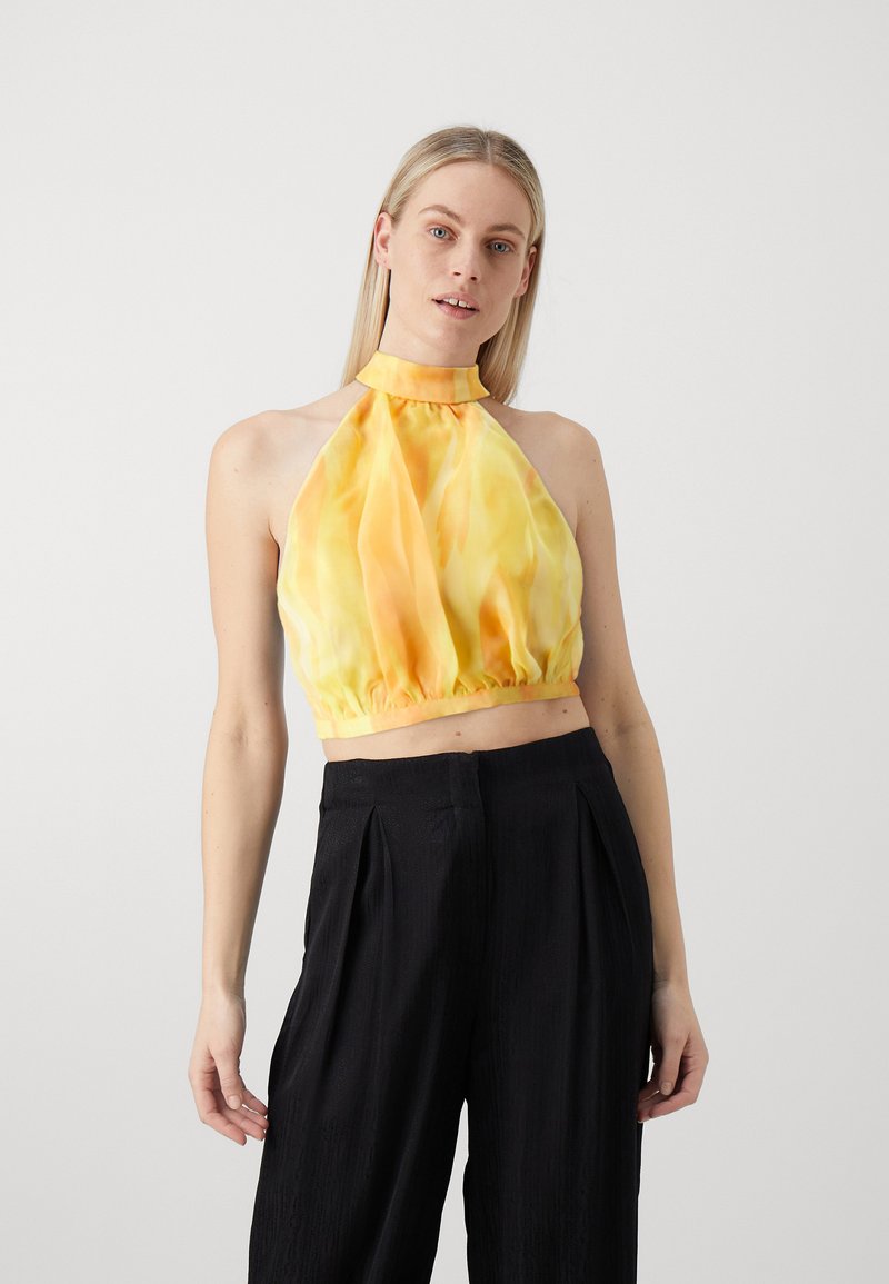 Gelbes Halfter-Crop-Top mit einem strukturierten, gerafften Saum. Verfügt über einen hohen Kragen und fließenden Stoff; kombiniert mit schwarzen hoch taillierten Hosen.