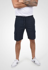 Shorts cargo bleus marine avec une taille élastique, des poches avant et des poches cargo sur les côtés. Fabriqués en tissu tissé avec une texture lisse.