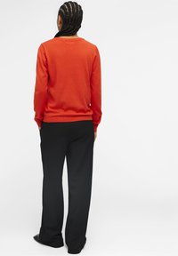 Suéter rojo de manga larga y cuello redondo, combinado con pantalones negros. Textura suave y corte relajado.