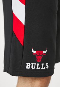 Shorts neri con accenti a zig-zag rossi e bianchi, con un logo di un toro rosso e il testo "BULLS" stampato in bianco vicino all'orlo.