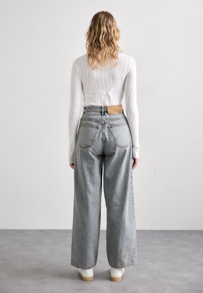 Lys grå vidde bukser med en indsnævret talje, med et læderpatch på bagsiden. Stylet med en hvid ribbet langærmet top.