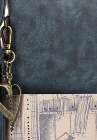 Schwarz strukturiertes Material mit einer hellbraunen Basis, das ein Skizzenmuster, einen metallischen herzförmigen Akzent und einen Hummerverschluss aufweist.