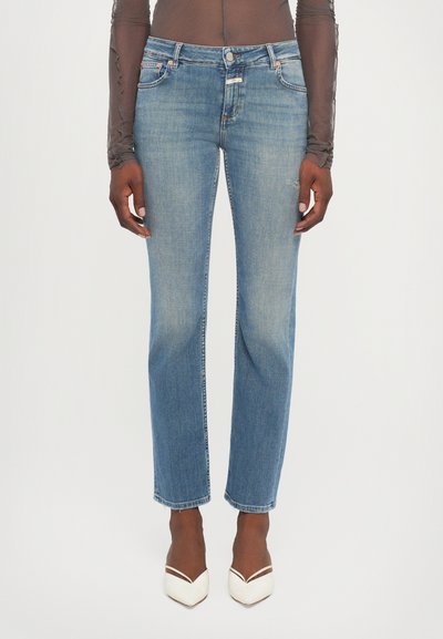 Jeans in denim blu chiaro con taglio dritto, fronte sbiadito, cinque tasche e dettagli cuciti. Abbinati a tacchi bianchi a punta.