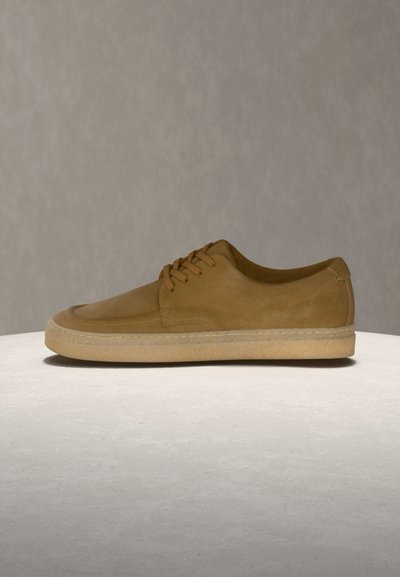 Zapatilla deportiva de cuero marrón con punta redondeada, costuras mínimas y diseño con cordones. Suela de goma marrón claro con agarre texturizado.