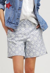 Jasnoniebieskie spodenki w wzory o geometrycznym designie, wykonane z miękkiego materiału. Charakteryzują się luźnym krojem i bocznymi kieszeniami.