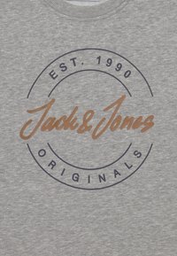 Šedá mikina s kulatým logem; zahrnuje "Jack & Jones" hnědým kurzívou a "EST. 1990" modrým textem, s hladkou strukturou.