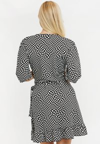 Vestido negro ceñido con un patrón de puntos blancos, mangas abullonadas cortas y un borde rizado. El material parece ligero y fluido.