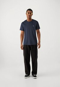 Navyblauw katoenen T-shirt met een ronde hals en korte mouwen; zwarte, wijd uitlopende broek; zwarte sneakers; accessoires omvatten een zonnebril.