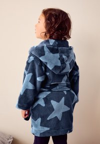 Fleece badekåbe i marineblå med lyseblåt stjernemønster, udstyret med hætte, bælte og lange ærmer, der giver en blød tekstur.