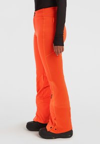 Oranje skibroek met contrasterende stiksels, een hoge tailleband en verstelbare manchetten, gemaakt van een flexibel, weerbestendig materiaal.