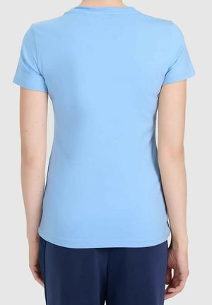 Persoon die een effen lichtblauw T-shirt met korte mouwen en donkerblauwe broek draagt, gezien van achteren tegen een lichte achtergrond.