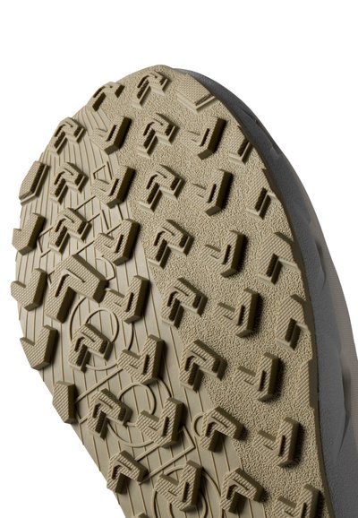 Semelle de chaussure avec un motif de traction détaillé, comportant des lugs géométriques en caoutchouc brun clair. Surface texturée avec des crêtes et des rainures visibles.