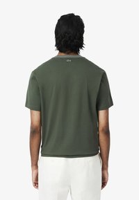 Donkergroen t-shirt met korte mouwen, gemaakt van katoen, met een ronde hals en een Lacoste-logo op de achterkant, netjes afgewerkt op de taille.