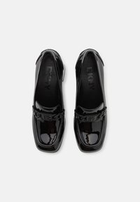 Mocassins en cuir verni noir avec un bout carré, arborant un accent de chaîne décoratif et un logo embossé discret sur la semelle intérieure.