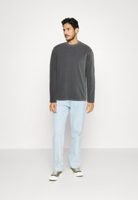 Camisa gris de manga larga hecha de un tejido suave, con cuello redondo y corte recto. Combinada con jeans azul claro y zapatillas verdes.