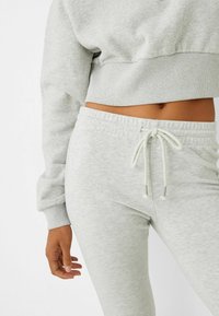 Felpa grigia cropped con cintura a costine e pantaloni coordinati in felpa con coulisse elastica e texture morbida.