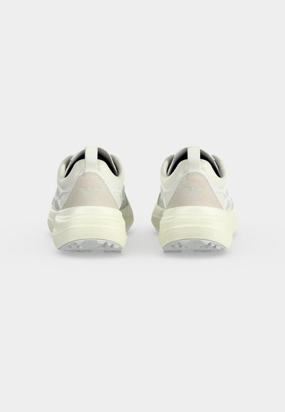 Paire de baskets blanches et beiges vues de dos avec des semelles épaisses et des languettes en boucle sur un fond clair uni.