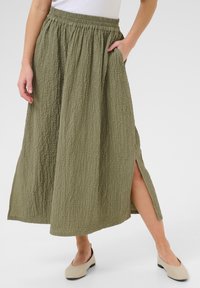 Olijfgroene, textuur maxi rok met een elastische tailleband, zijsplitsen en zakken. Gecombineerd met crèmeskleurige flats voor een casual stijl.