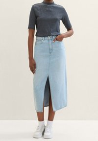 Ljusblå jeanskjol med en slits framtill, kombinerad med en svart- och vitrandig kortärmad topp och vita sneakers.