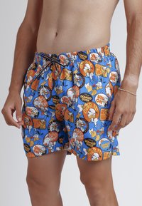 Bañador azul con un estampado de dibujos animados de Pato Donald, con acentos naranjas, blancos y negros. Cintura elástica con cordón.