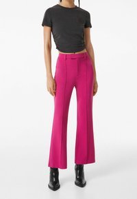 Różowe spódnice w kształcie dzwonów o gładkiej fakturze, wysoki stan i dwa przednie szwy; połączone z czarnym krótkim t-shirtem i czarnymi botkami za kostkę.