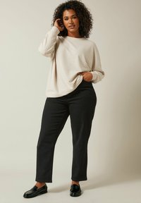 Maglia a manica lunga beige chiaro a coste abbinata a pantaloni slim-fit neri e mocassini neri lucidi. Design semplice e colori neutri.