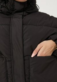 Giacca a vento nera con colletto alto, chiusura con zip sul davanti e tasche laterali. Il tessuto è liscio con una texture a trapunta.