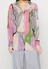 Blouse élégante et colorée arborant un motif avec des formes roses, vertes, grises et violettes. Devant boutonné et manches longues. Tissu doux.