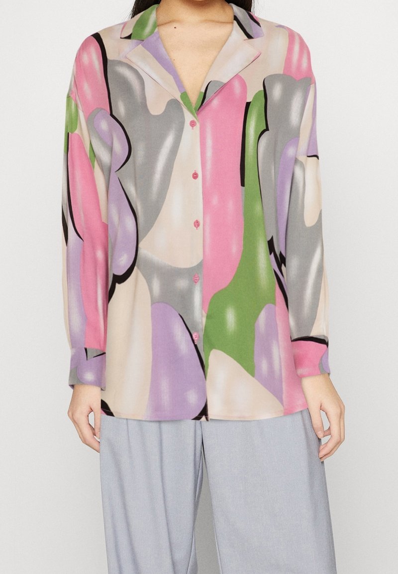 Blouse élégante et colorée arborant un motif avec des formes roses, vertes, grises et violettes. Devant boutonné et manches longues. Tissu doux.