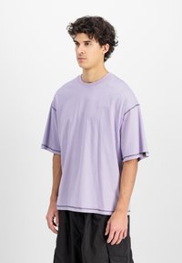 Tricou oversized de lavandă, fabricat din bumbac moale, având cusături contrastante pe mâneci și o etichetă mică la tiv.