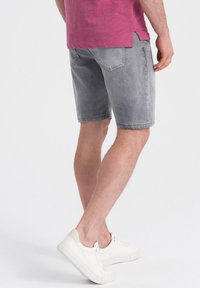 Pantalones cortos de mezclilla gris con un corte clásico, que presentan una textura suave, un ligero desvanecimiento y bolsillos traseros, combinados con zapatillas blancas.
