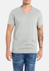 Lichtgrijze T-shirt met korte mouwen en V-hals, gemaakt van zachte stof. Heeft een relaxte pasvorm en een eenvoudig ontwerp, gecombineerd met blauwe spijkerbroek.
