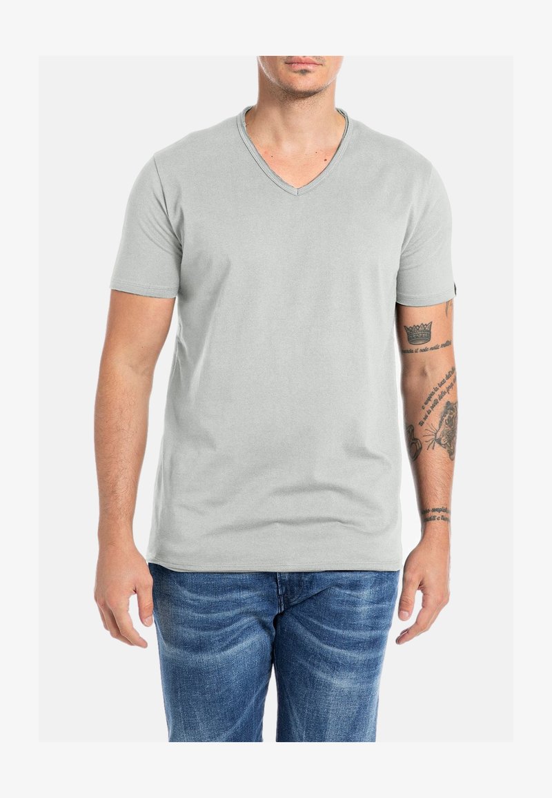 Jasnoszara, krótko rękawowa koszulka V-neck wykonana z miękkiej tkaniny. Posiada luźny krój i jednolity design, w połączeniu z niebieskimi dżinsami.