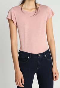 Light pink short-sleeve top with a round neckline, paired with dark blue denim jeans featuring front pockets and a button closure.