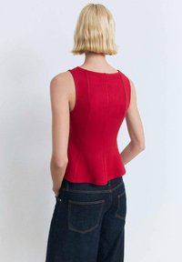 Red fitted sleeveless top with a peplum hem, made of textured fabric. Visible seams highlight the design, paired with dark denim pants.