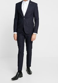 Donkerblauw krijtstreep pak met een op maat gemaakte blazer en nauwsluitende broek, gecombineerd met een wit overhemd en zwarte nette schoenen.