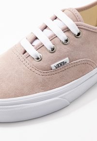 Sneaker Vans in scamosciato rosa chiaro con lacci bianchi, occhielli metallici e suola in gomma bianca su uno sfondo bianco.