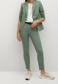 Jasnozielona marynarka i pasujące spodnie wykonane z gładkiego materiału. Bielizna pod spodem, w zestawie z jasnymi sneakersami.