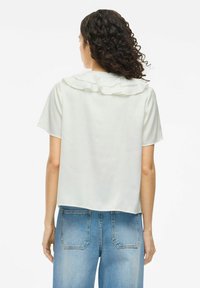 White short-sleeve blouse with a ruffled collar, smooth texture, and a cropped design, paired with light blue high-waisted jeans.