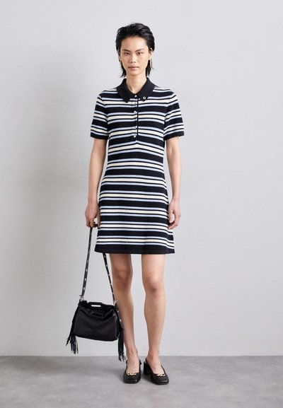 Black and white striped polo dress with short sleeves, buttoned collar, and a straight cut. Paired with a small black bag and flat shoes.