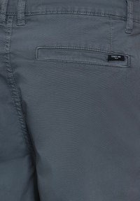 Shorts en tissu gris avec une texture lisse, dotés d'une poche arrière avec une étiquette noire portant l'inscription "STREET ONE". Les coutures sont visibles le long des coutures.