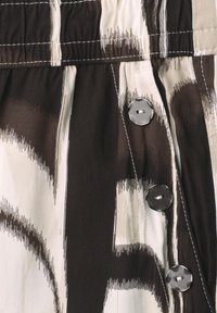 Close-up of brown and beige patterned fabric with three black buttons and visible white stitching on gathered waistband.