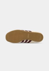 Sneaker con una toma beige, dotato di tre strisce bordeaux e una suola in gomma testurizzata con un motivo a zigzag.