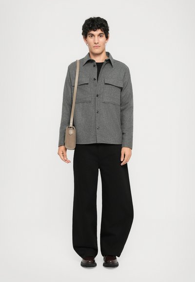 Grey wool blend button-up shirt with two chest pockets, paired with black wide-leg pants and brown shoes. Sling bag worn crossbody.