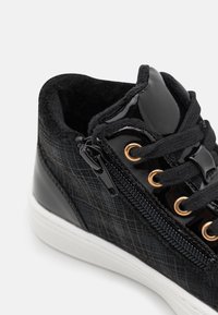Zapatillas altas negras con una tela de cuadros texturizada y acentos de cuero charol brillante. Cuenta con ojales dorados y una cremallera lateral para un fácil acceso.
