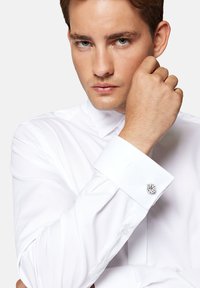 Biała koszula z sztywnym kołnierzykiem i mankietami na guziki, z dekoracyjnym spinką do mankietów. Gładki materiał o wypolerowanym wykończeniu.