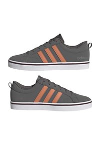 Baskets Adidas basses grises avec trois bandes orange sur les côtés, lacets noirs, semelles blanches et languettes à l'arrière.