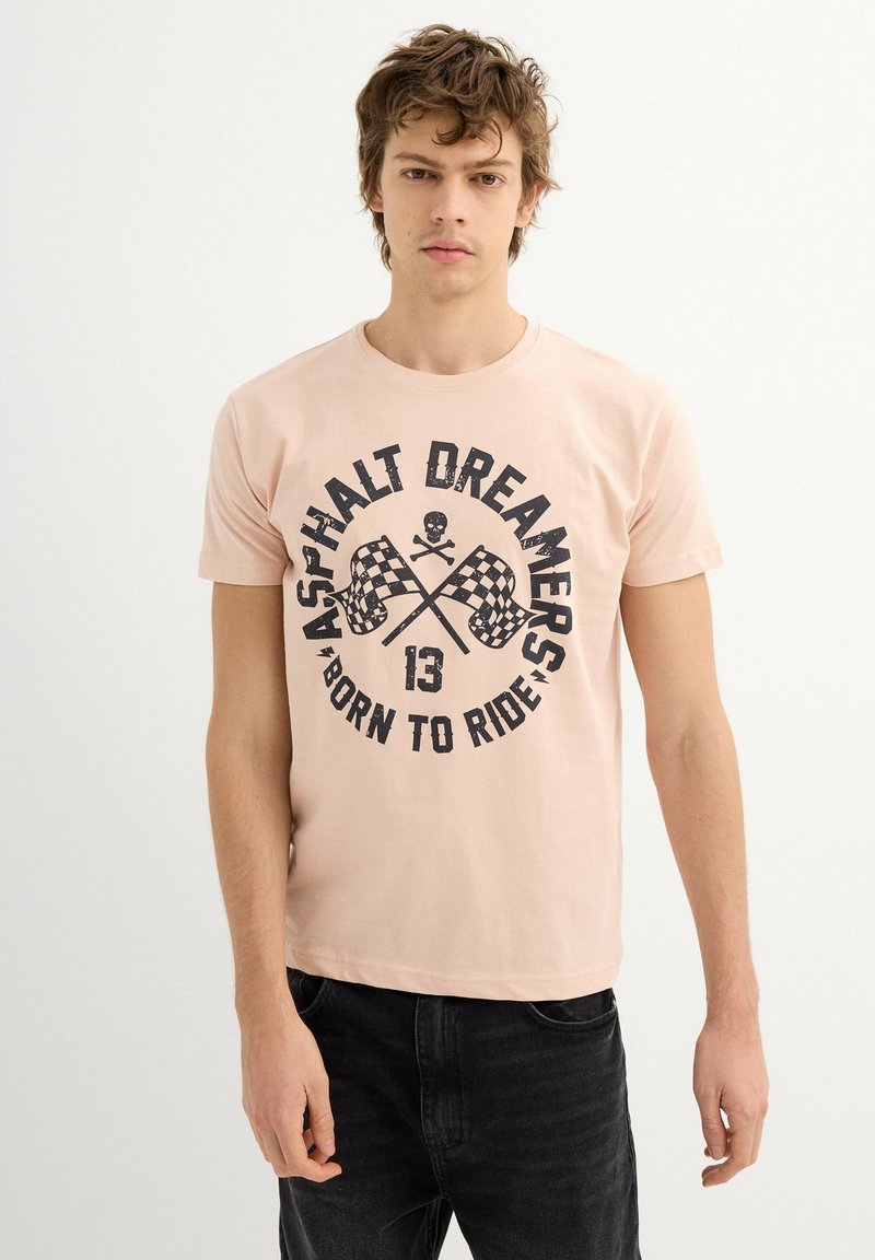 Camiseta de color rosa claro con estampado gráfico negro que presenta banderas a cuadros entrecruzadas y texto, cuello redondo, mangas cortas y material de algodón.