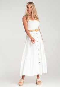Biała maxi sukienka z warstwowym wzorem, żebrowanym topem i przyciskami z przodu. Połączona z beżowym paskiem i plecionymi sandałami na platformie.
