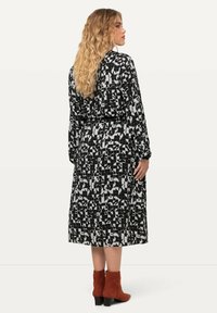 Schwarzes und weißes gemustertes Kleid mit langen Ärmeln, tailliertem Schnitt und knöchellangem Saum, kombiniert mit orange-roten Stiefeletten.